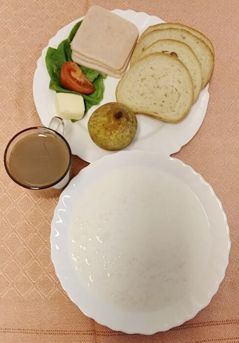 zupa mleczna, kubek z kawą oraz talerzyk z wędliną, masłem, pieczywem, sałatą, pomidorem i gruszka.