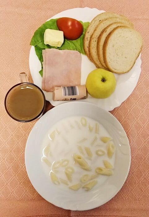 talerz z zupą mleczną oraz talerz z wędliną, pasztetem, pomidorem, sałatą, masłem oraz jabłko