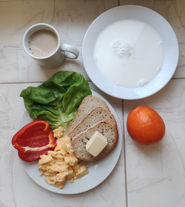 Zupa mleczna, jajecznica, warzywai i chleb z masłem oraz kubek z kawą i pomarańcza